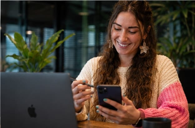 Nata van Houdt checking a design on her phone beside a laptop